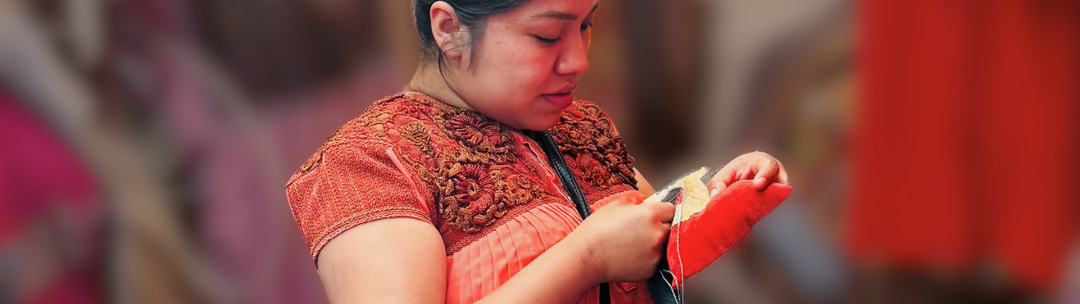 Lumily artisan wearing a traditional embroidered blouse, focused on crafting a handmade textile piece against a blurred background of warm tones