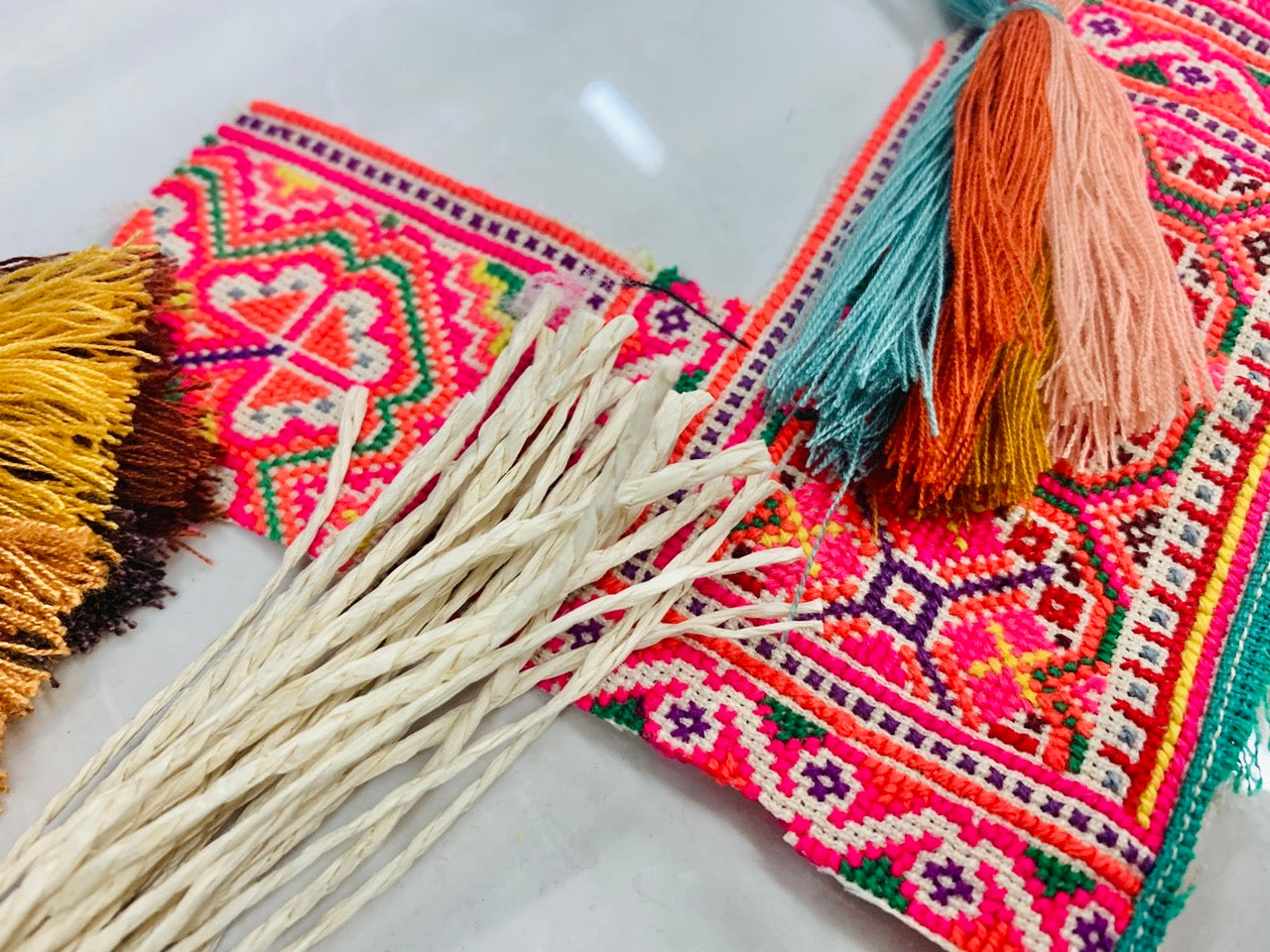 A person holding a colorful embroidered clutch with vibrant red, pink, and orange tassels, featuring intricate geometric patterns.