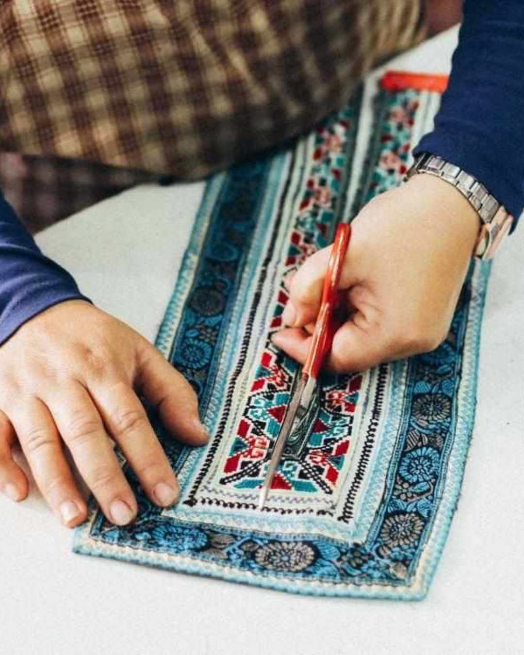A person holding a colorful embroidered clutch with vibrant red, pink, and orange tassels, featuring intricate geometric patterns.