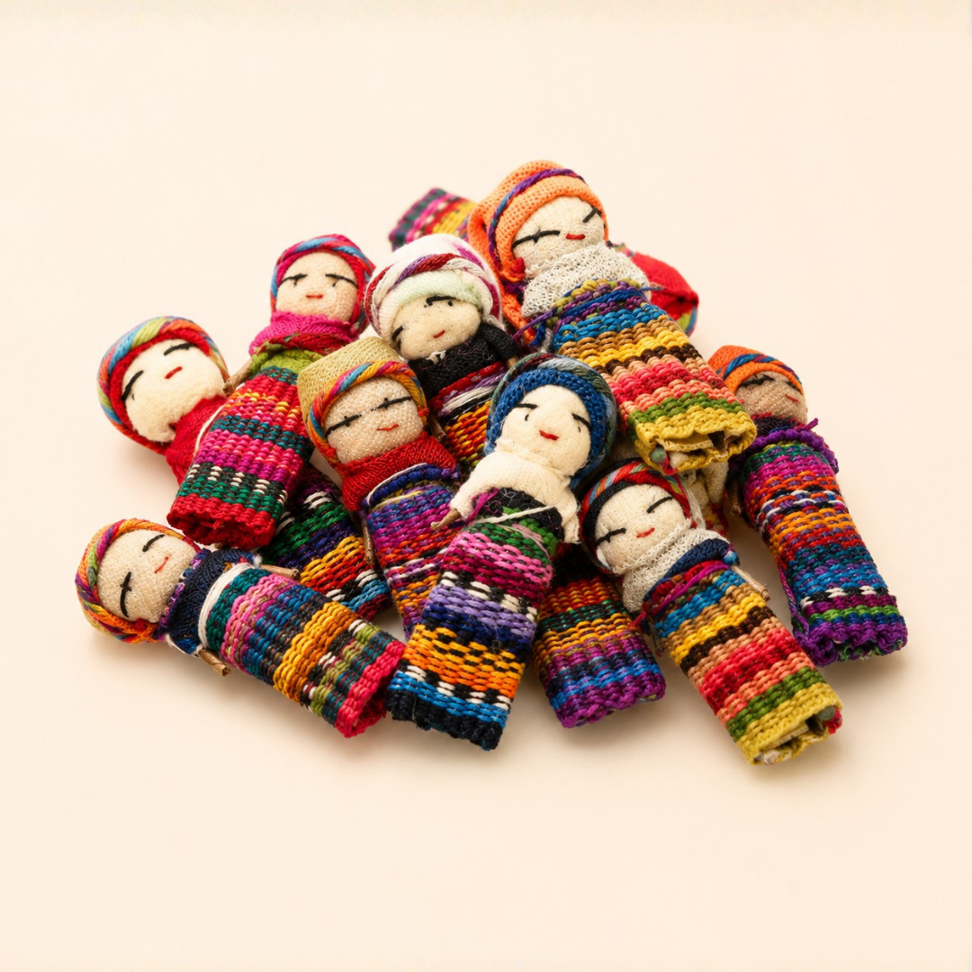 A pile of colorful handmade Guatemalan woven worry doll toys with embroidered faces, arranged on a plain light beige background.